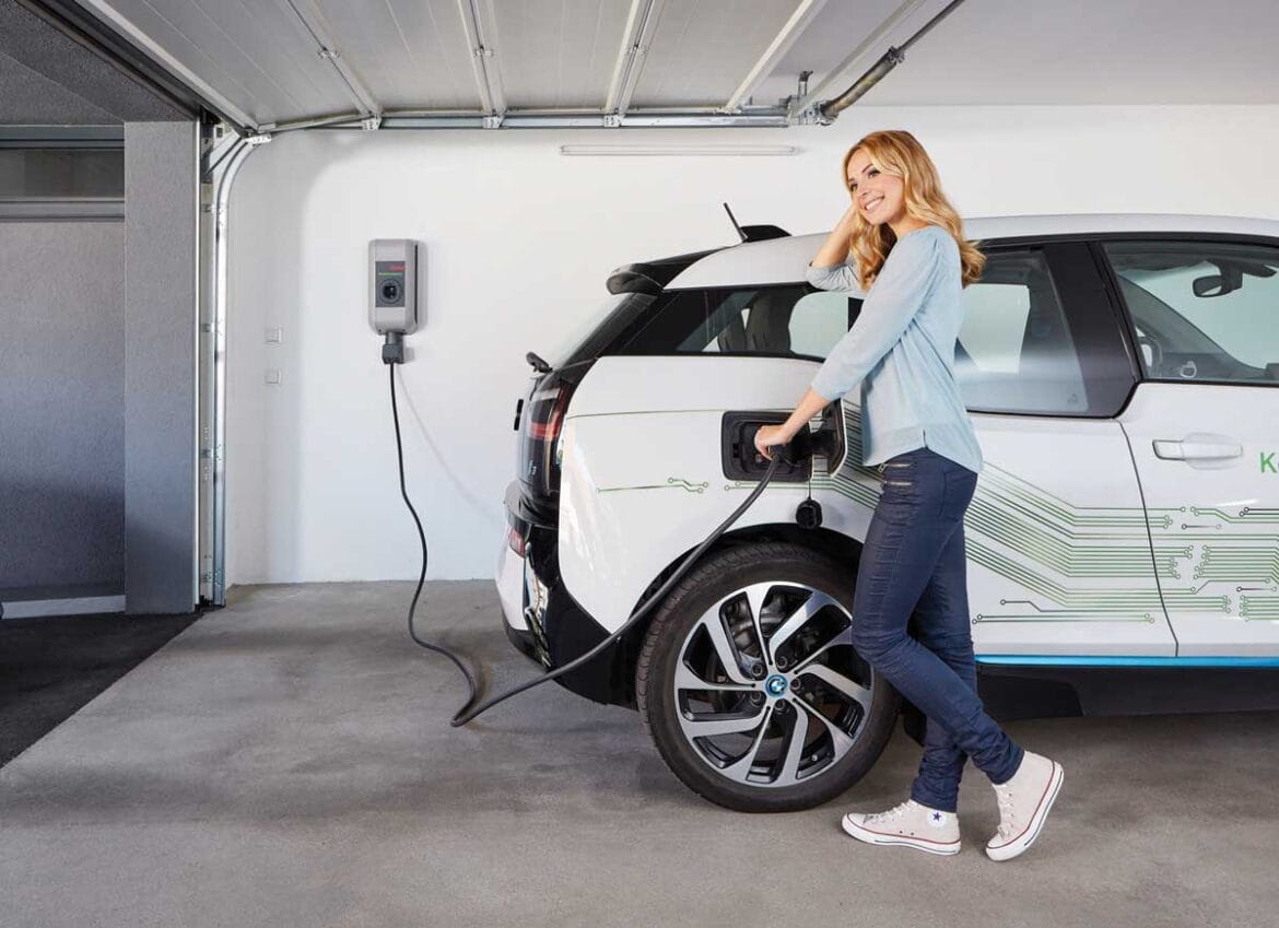 Ženska polni električni avto v domači garaži z nameščeno stensko polnilnico za električni avto