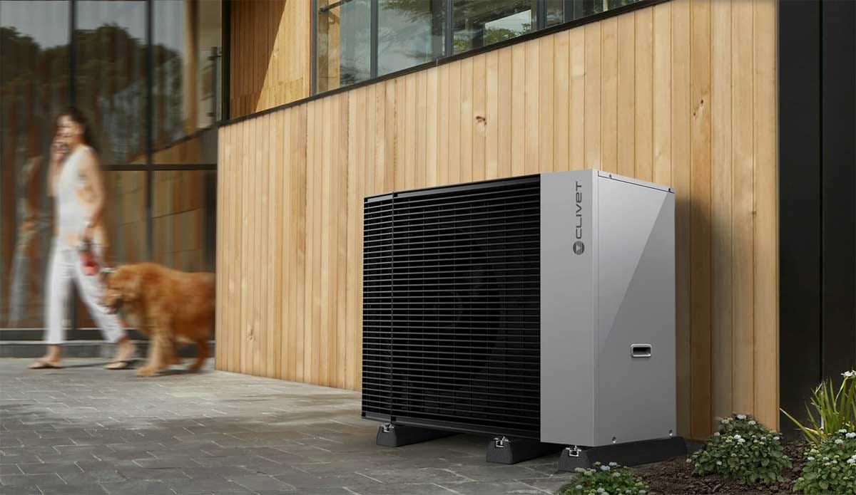 Toplotna črpalka Clivet Edge Pro ob hiši z leseno fasado, mimo gre ženska s psom