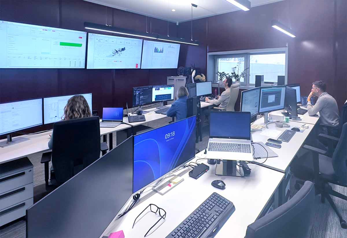 Nadzorni center za monitoring sončnih elektrarn z več zasloni in strokovnjaki, ki spremljajo delovanje sistemov v realnem času